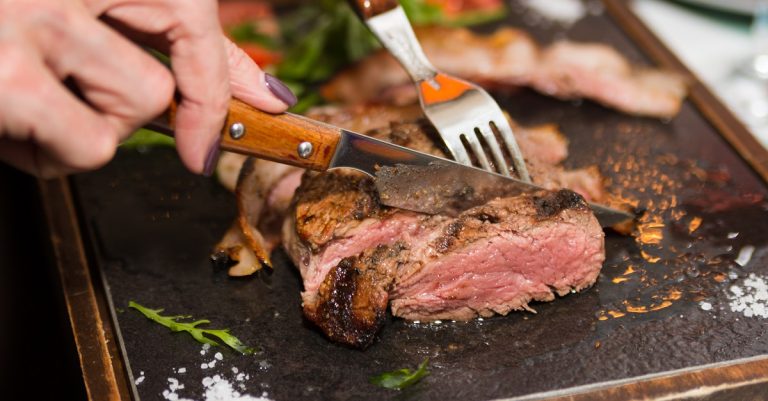 Woman hand holding knife and fork cutting grilled beef steak